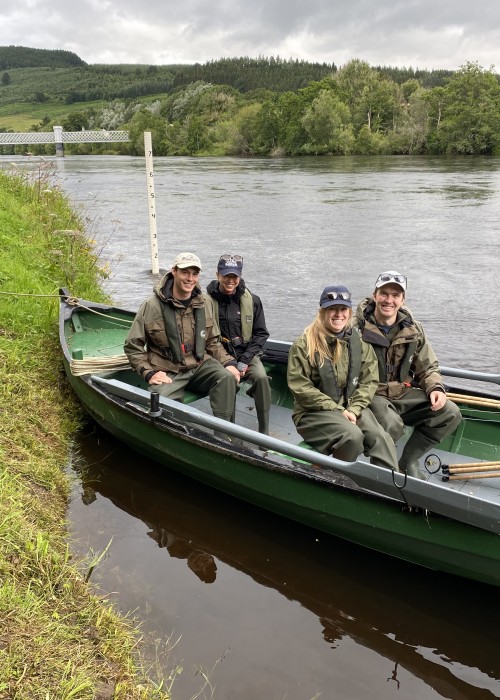 Here's 2 young couples ready in the boat to be taken down river to the superb salmon fishing locations near the River Tummel mouth area. You can see the hand carved black painted digits on the while plastic lumber water gauge behind the boat and the old grey painted iron railway bridge at Logierait in the distance.